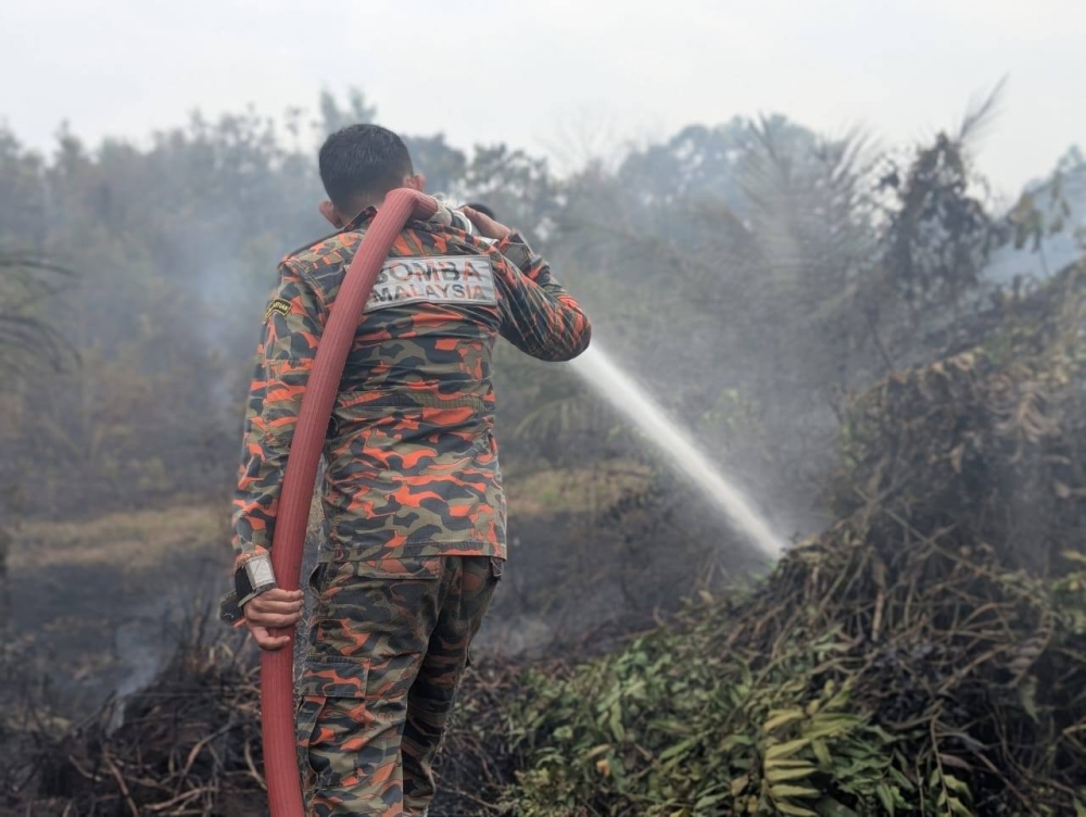 A firefighter from the Fire and Rescue Department of Malaysia works to douse a stubborn peatland blaze in Johor, where underground embers can smoulder for weeks despite surface flames dying out. — Picture via Facebook/bombajdt