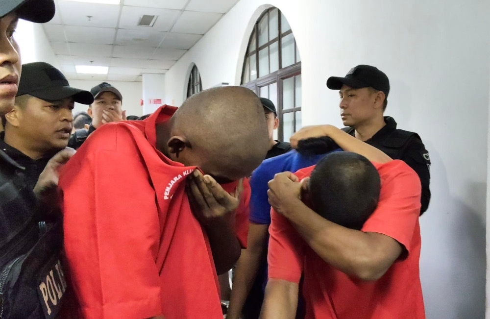 Two of the 12 suspects being escorted by policemen at the Johor Bahru court complex today. All 12 were later charged for allegedly being members of a organised criminal organisation, February 12, 2026. — Picture by Ben Tan