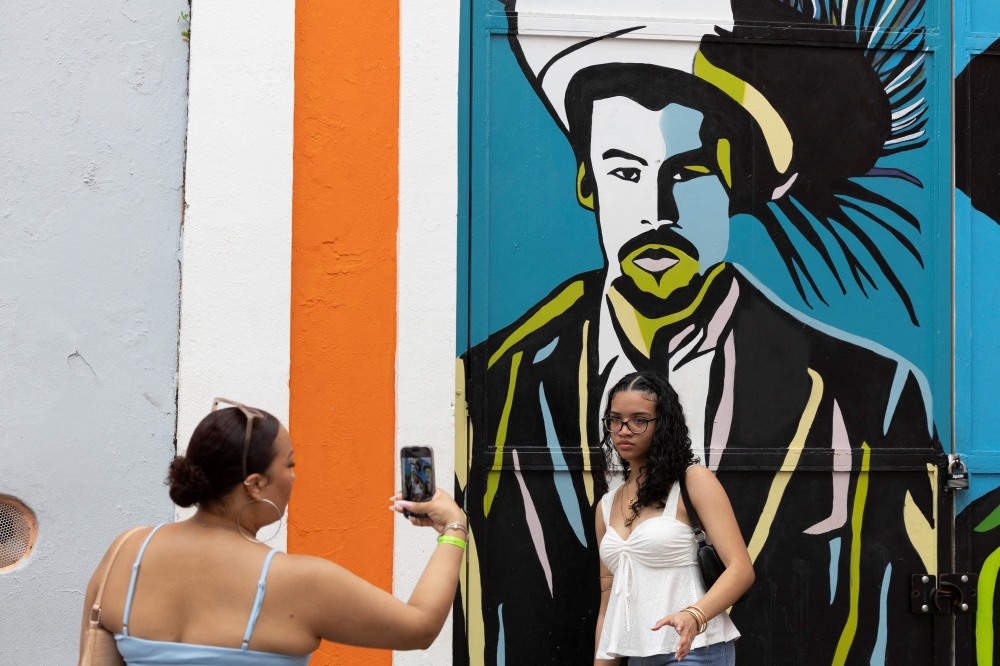 A woman takes a photo of another woman posing in front of a mural depicting Puerto Rican singer Bad Bunny in Old San Juan on February 10, 2026. — Reuters pic