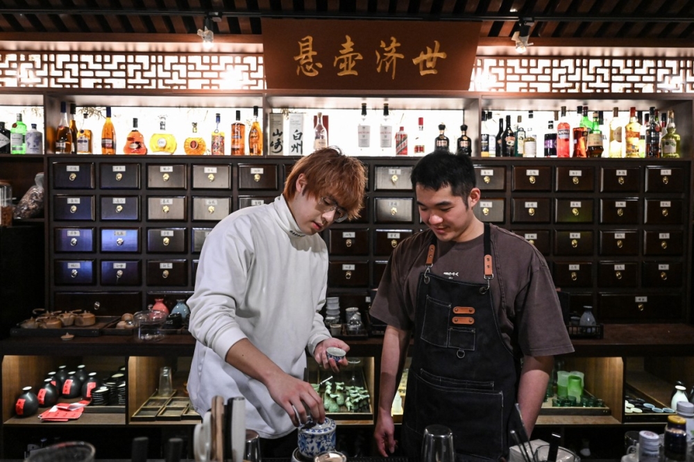 Bar owner Wu Siyuan (L) talking with a bartender in front of a plaque with the motto of Chinese medicine “Practice medicine to help the world” at a traditional Chinese medicine-themed cocktail bar in Shanghai. — AFP pic