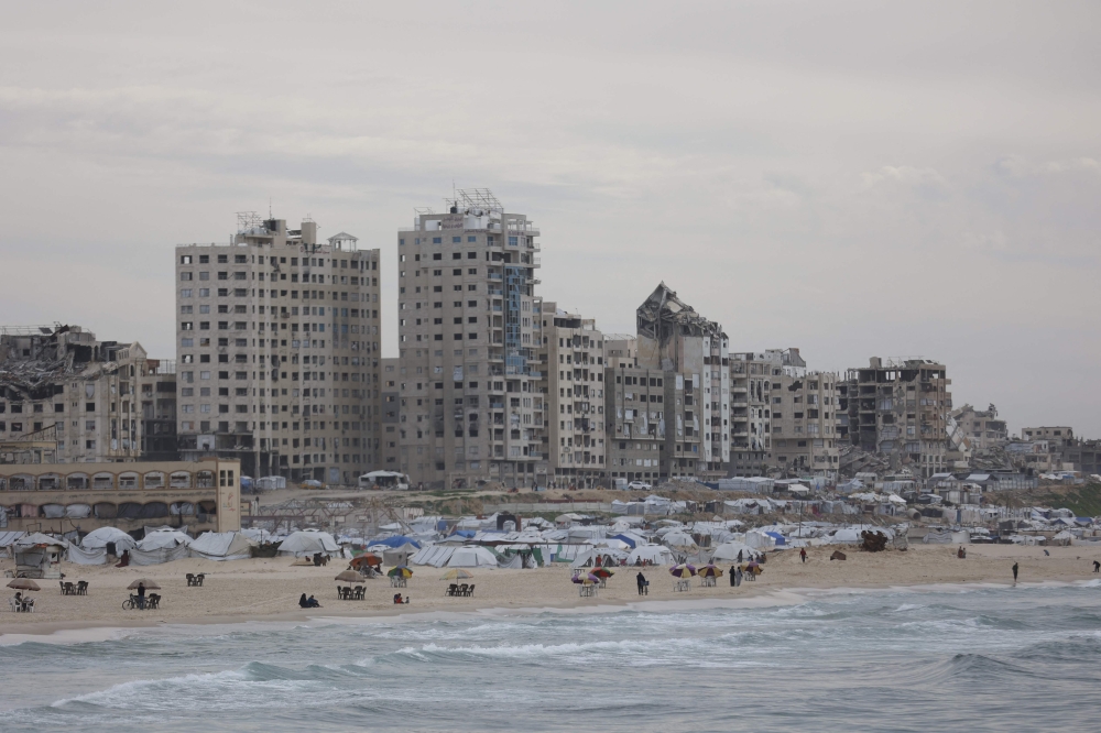 A picture taken on February 12, 2026 shows destroyed building and people gathered at the beach along the shore of the Gaza City. — AFP pic