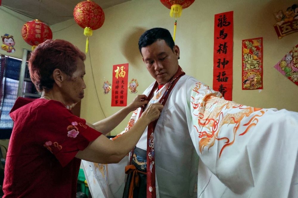 Chan Qi Yao, 33, is assisted by his mother, Arob Rattanaburi, 62, in arranging his ‘hanfu’ outfit at Kampung Batu Papan 2, Gua Musang.— Bernama pic  
