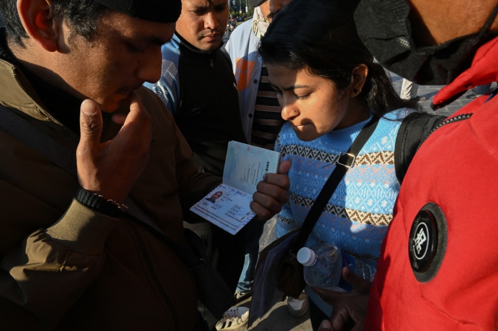 This photograph taken on January 21, 2026 shows Lalit Bishowkarma (L), son of migrant worker Rudra Bahadur Kami, looking at his father's passport with a relative as they wait for the arrival of Kami's body outside Tribhuvan International Airport in Kathmandu. — AFP pic