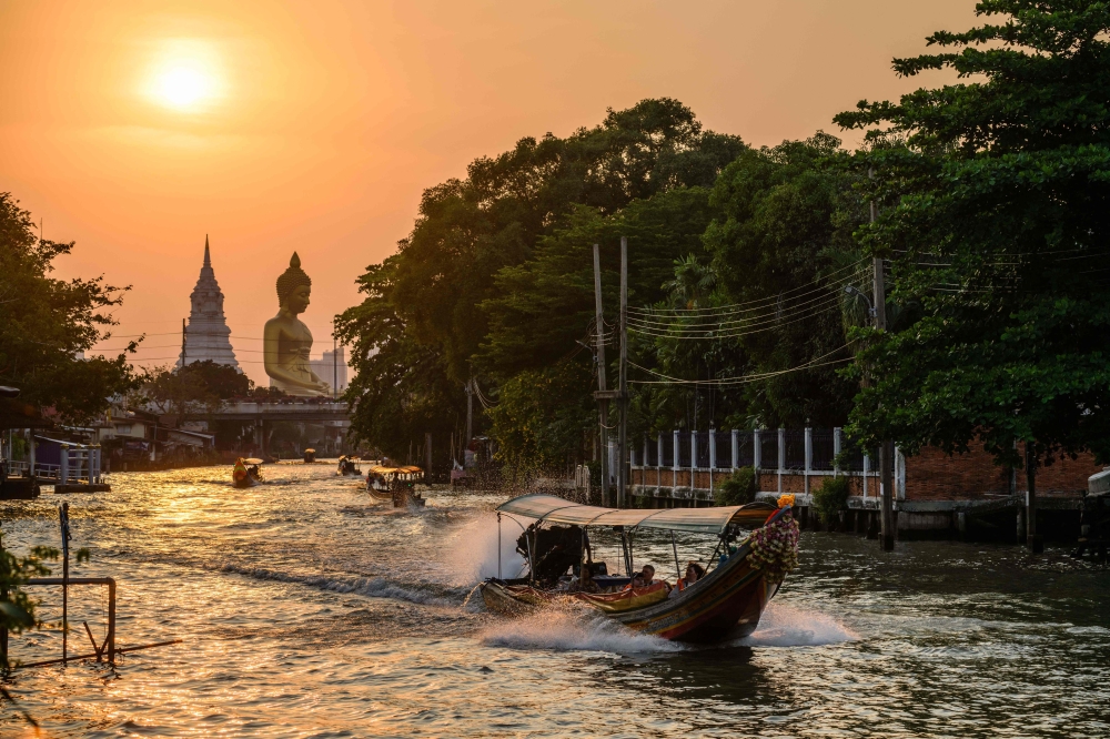 People ride boats in a canal as the sun begins to set behind the 69-metre tall giant Buddha statue of Wat Paknam Phasi Charoen temple (back, left) in Bangkok on February 16, 2026. A Thai court has sentenced a jailed activist lawyer to an additional two years and eight months in prison for insulting the monarchy at a rally in November 2020, a rights group said on Friday, bringing his combined sentence to more than 30 years. — AFP pic 