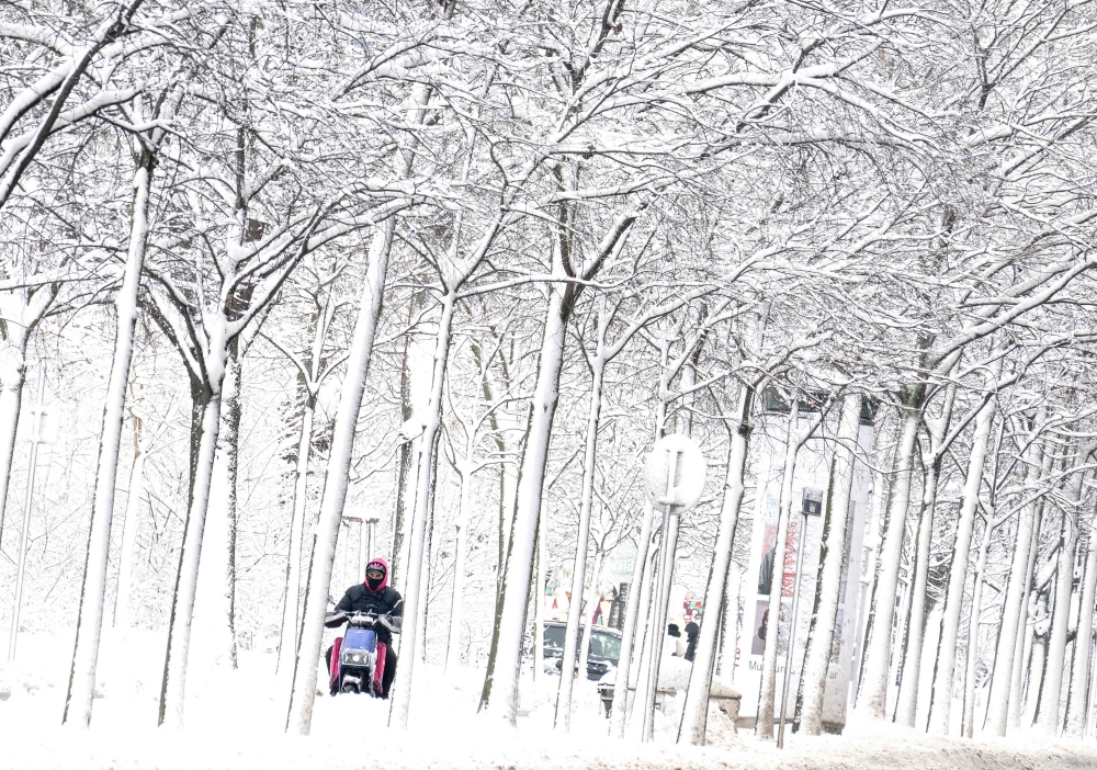 A food delivery person rides an electric scooter through the snow-covered Gaudenzdorfer Gürtel Boulevard as winter strikes Vienna, Austria, with snow and freezing temperatures yesterday. — AFP pic