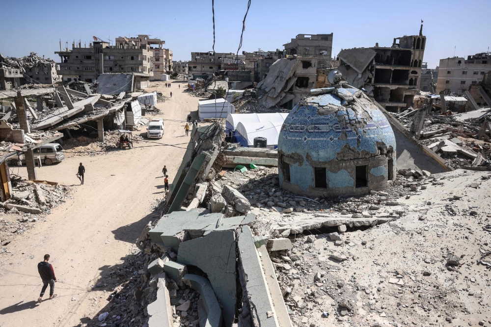Displaced Palestinians walk past the destroyed Al-Huda Mosque on the first Friday noon prayers of the holy month of Ramadan, in Khan Yunis in the southern Gaza Strip yesterday. — AFP pic