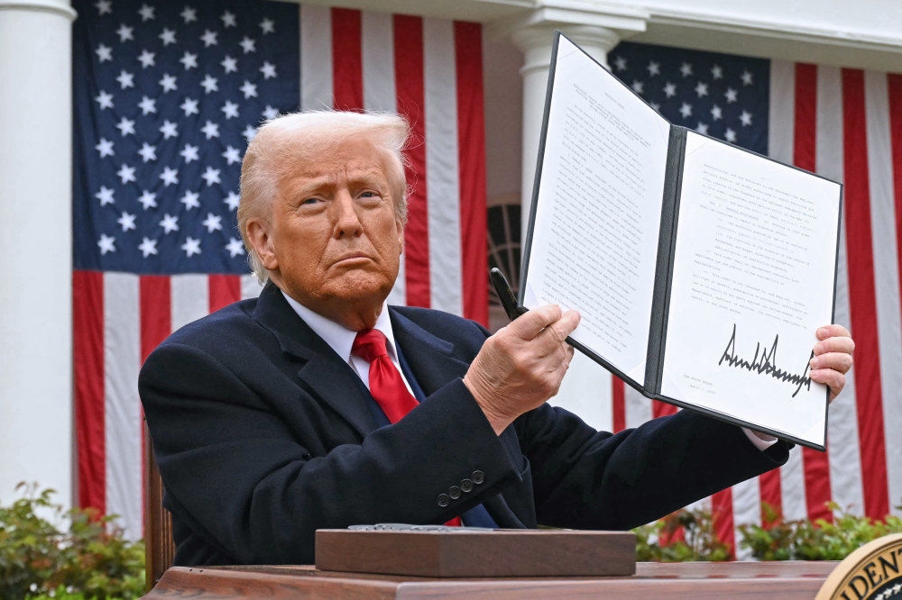 US President Donald Trump holds a signed executive order after delivering remarks on reciprocal tariffs at the White House in Washington, DC, on April 2, 2025. — Reuters pic