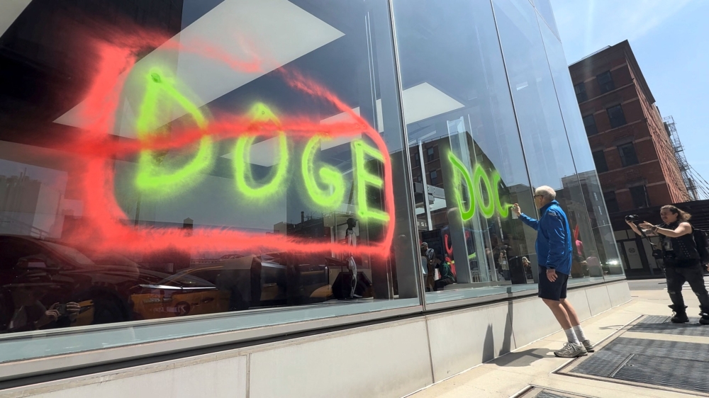 A man sprays paint graffiti against Elon Musk's Department of Government Efficiency (DOGE) on a Tesla showroom in New York, US yesterday, in this still image taken from video. —  AFP pic