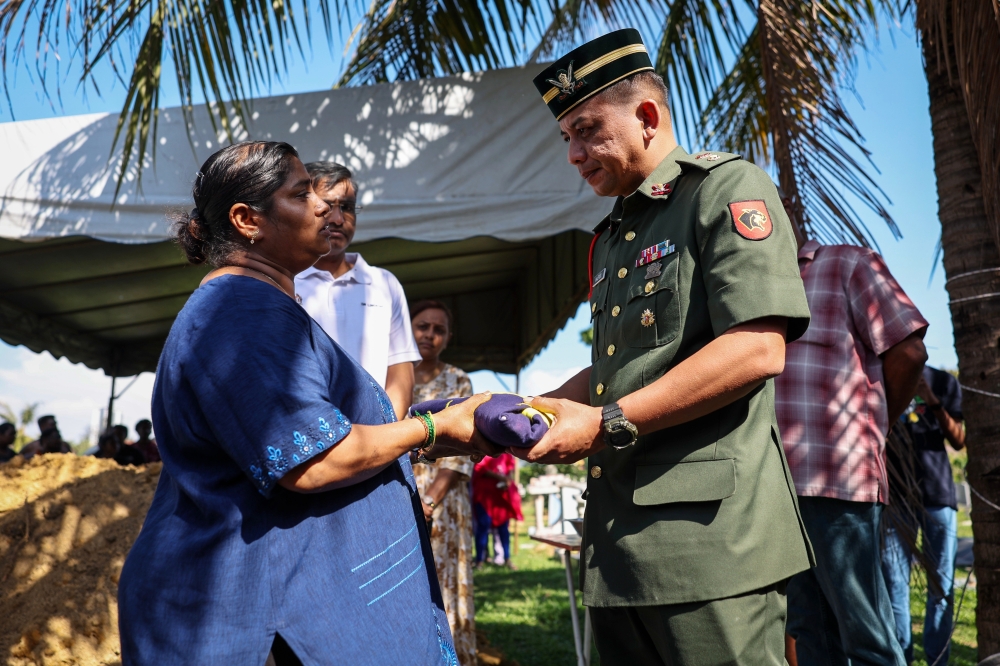 Commanding Officer of the 1st Regiment Royal Armoured Corps Lt Col Nazrol Abdullah (right) hands over the Jalur Gemilang to S. Usha, 52 (left), during the funeral of her son, the late Trooper K. Indiran, at Batu Lanchang Hindu Cemetery, George Town, February 21, 2026. — Bernama pic