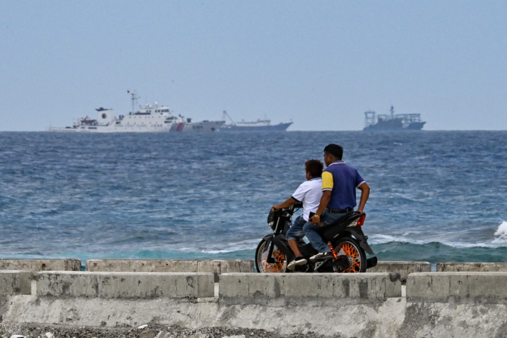 A China Coast Guard ship is seen as residents ride a motorcycle on Thitu Island in the South China Sea on February 21, 2026. — AFP pic 