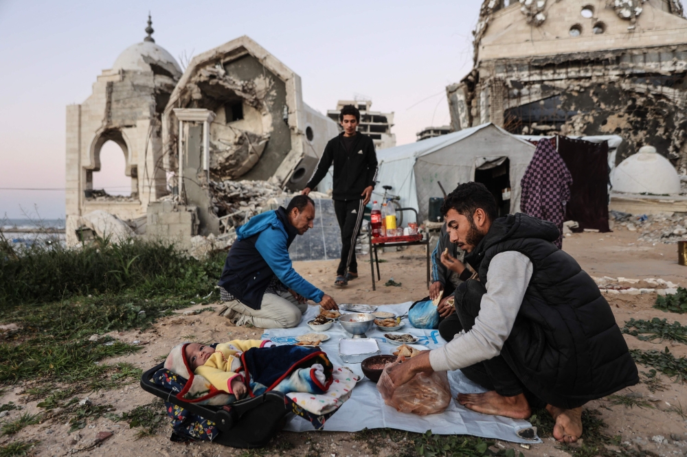 The displaced Palestinian al-Ghafir family gathers to sit together to break the dawn-to-dusk Ramadan fast during Iftar next to their tent, which is erected amid the ruins of the al-Hasayna Mosque in western Gaza City. — AFP pic