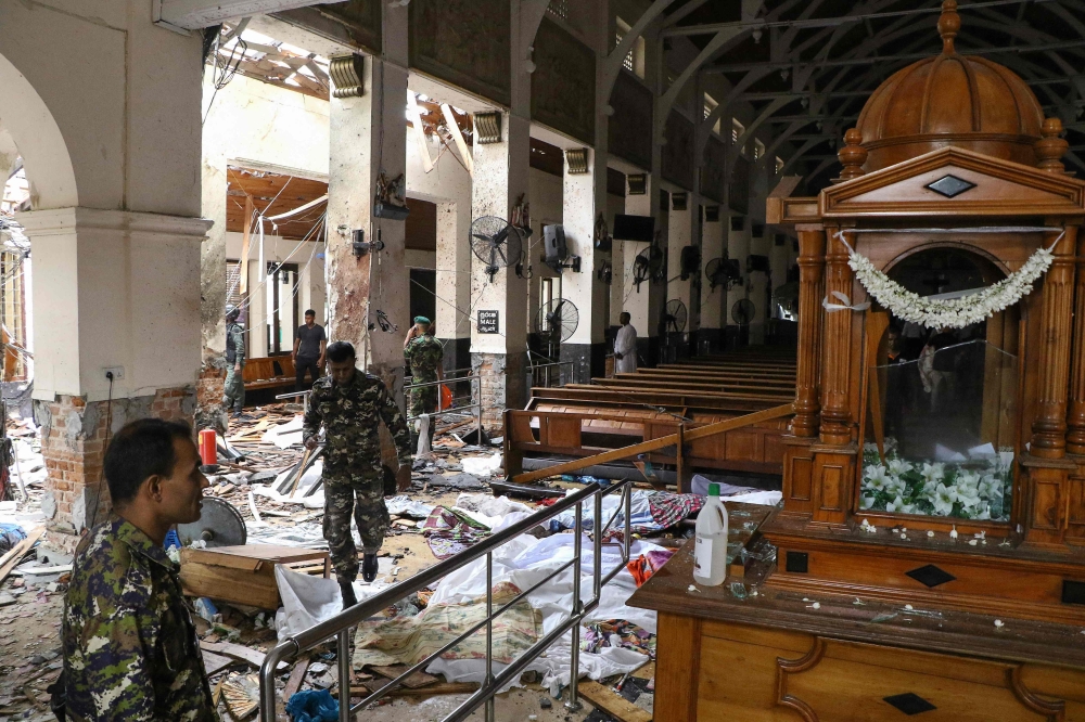 Sri Lankan security personnel walk past dead bodies covered with blankets amid blast debris at St. Anthony’s Shrine following an explosion in the church in Kochchikade in Colombo on April 21, 2019. — AFP pic