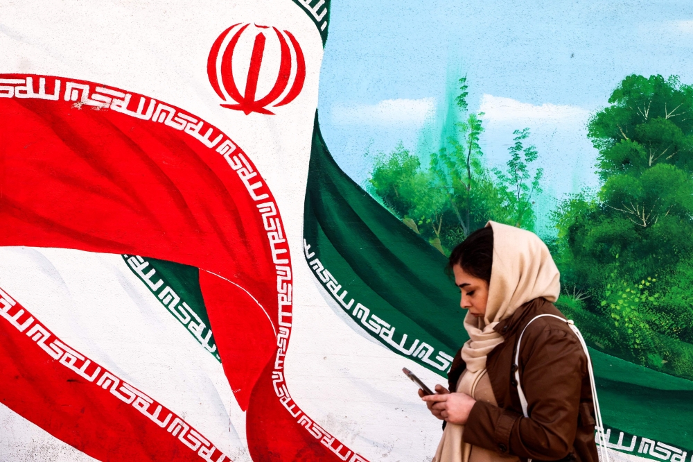 A woman walks past a mural of an Iranian flag in Tehran on February 22, 2026.  — AFP pic