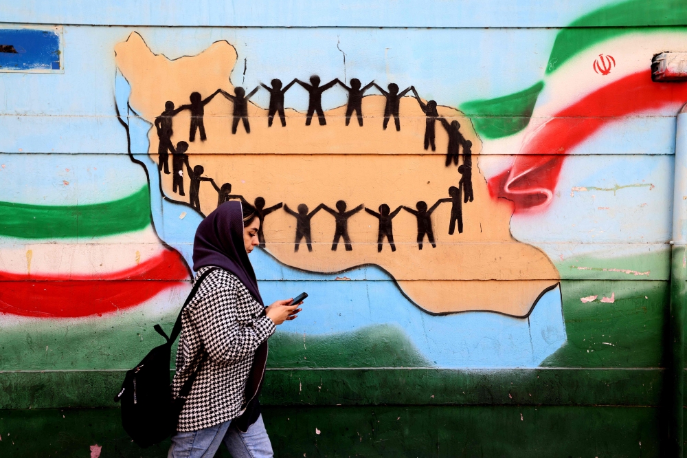 A woman walks past the flag and map of Iran painted on a wall in Tehran on February 25, 2026. — AFP pic 