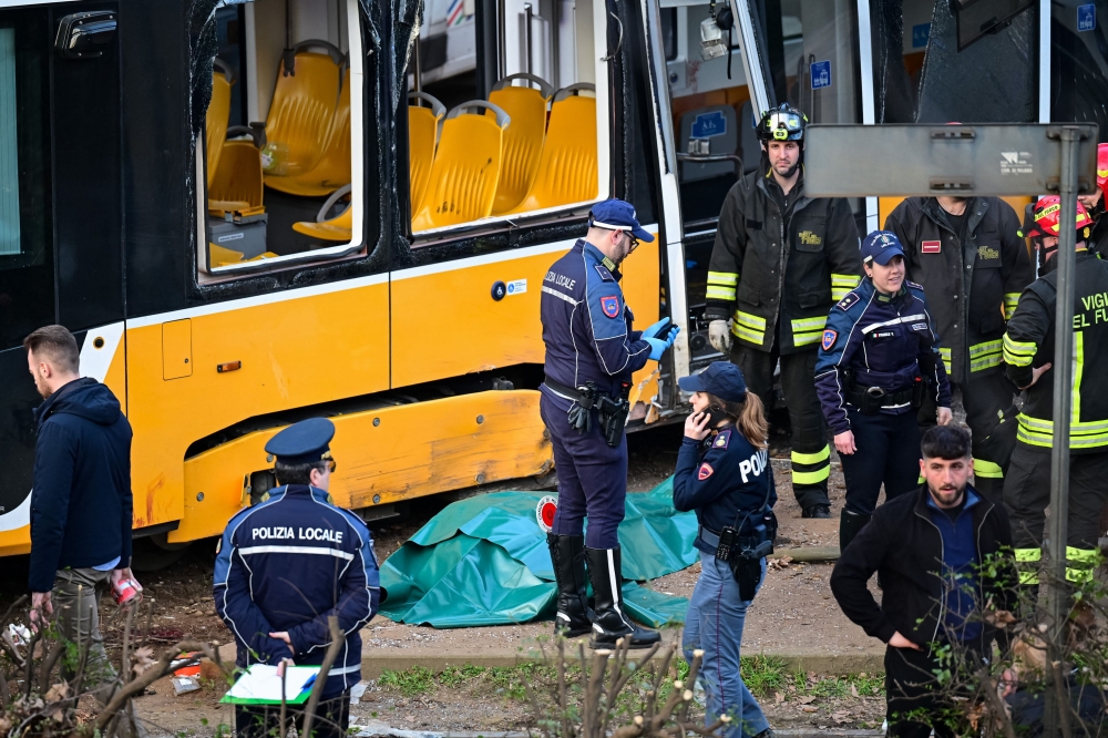 Italian police officers and firefighters stand next to a body bag at the site of a tram derailment in Milan on February 27, 2026. — AFP pic