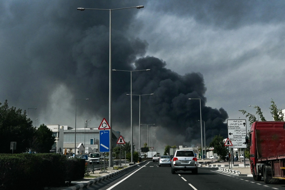 Motorists drive past a plume of smoke rising from a reported Iranian strike in the industrial district of Doha on March 1, 2026. — AFP pic