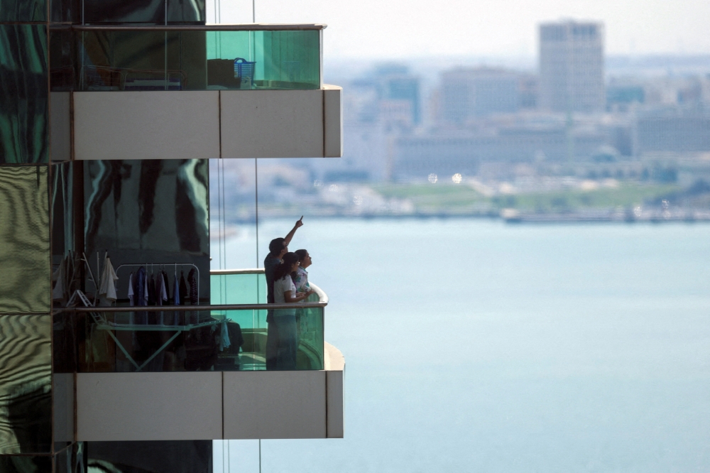 People in Doha watch from their balcony following explosions after Qatar’s Defence Ministry says it has downed missiles targeting the country on February 28, 2026. — Reuters pic