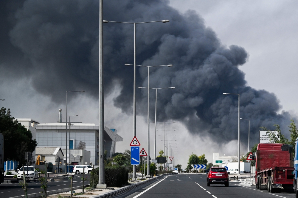 Motorists drive past a plume of smoke rising from a reported Iranian strike in the industrial district of Doha on March 1, 2026. — AFP pic