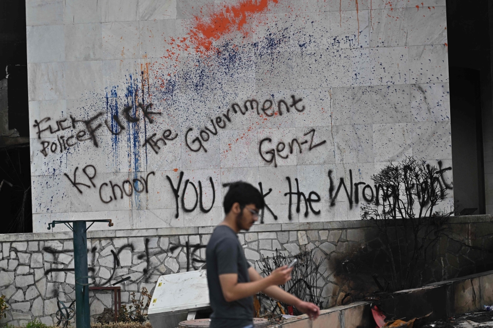 A man uses a phone as he walks past a graffitied wall on the facade of the torched Parliament building in Kathmandu on September 14, 2025. — AFP pic