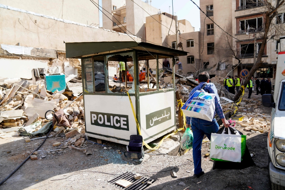 This picture obtained from Iran's ISNA news agency, shows an Iranian man carrying bags as he walks past debris from a destroyed building following a missile strike on a neighborhood of the Iranian capital Tehran on February 28, 2026. — Amir Kholousi/ISNA/AFP pic