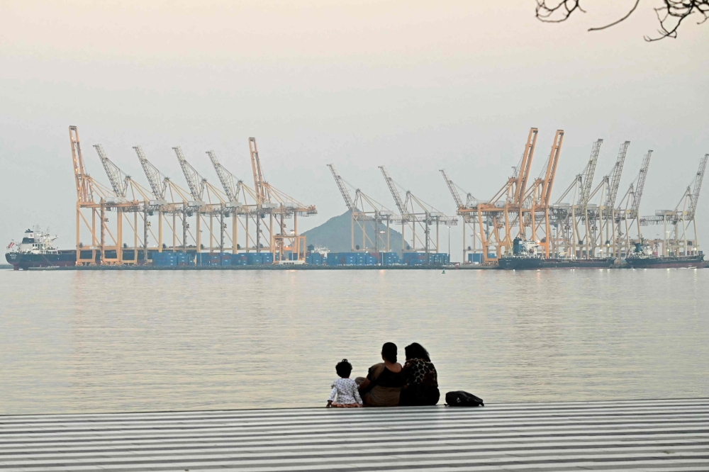 A family sits against the backdrop of a dockyard off coast city of Fujairah, in the Strait of Hormuz in the northern Emirate February 25, 2026. — AFP pic