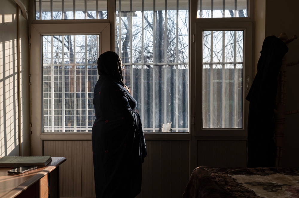 An Afghan hospital medic, who studied public relations and journalism before universities were closed to women, stands next to a window inside a house in Afghanistan on February 17, 2026. — AFP pic