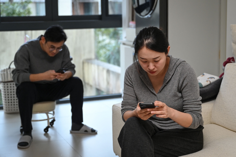 Wang Yifan (right) and her husband check their phones at their home in Shanghai on February 9, 2026. — AFP pic