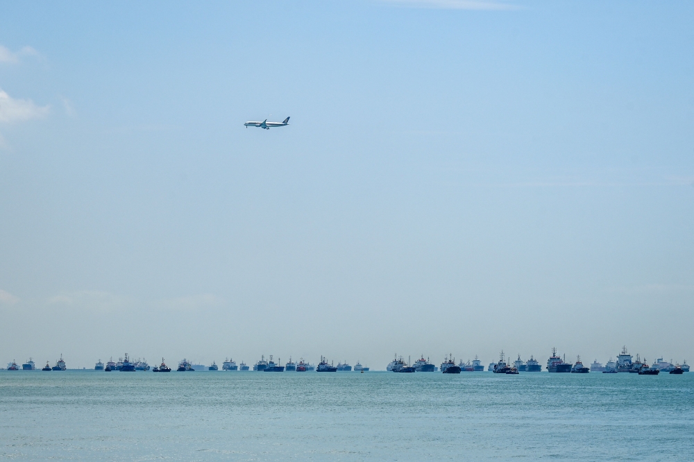 A passenger plane flies over vessels anchored along the Singapore straits in Singapore on February 26, 2026. The Singapore Foreign Affairs Ministry and its overseas missions in the Middle East are conducting a survey to gauge the level of interest among Singaporeans in the region for assisted departure arrangements amid ongoing airport closures. — AFP pic 