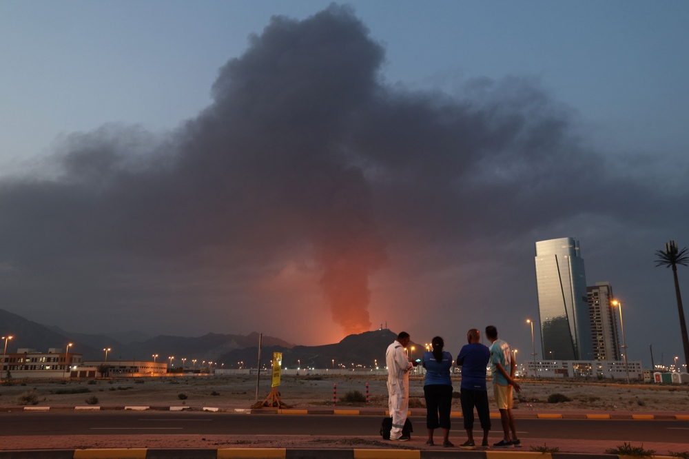 Foreign workers look at a tall plume of black smoke ascends following an explosion in the Fujairah industrial zone on March 3, 2026. An ATP Challenger tennis tournament in the UAE’s Fujairah was cancelled yesterday after play was interrupted earlier in the day because of drone strikes on nearby oil refineries. — AFP pic 