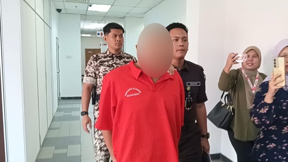 A 43-year-old security guard is escorted out of the Johor Bahru Sessions Court after being sentenced to 21 years’ jail and 24 strokes of the cane for 13 sexual offence charges. His face is obscured to protect the victim’s identity. — Picture by Ben Tan