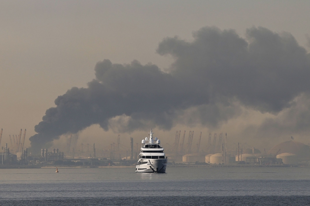 A yacht sails past a plume of smoke rising from the port of Jebel Ali following a reported Iranian strike in Dubai on March 1, 2026. — AFP pic