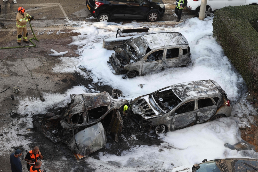 Israeli security forces and emergency personnel stand next to the wreckage of cars at a site struck by a projectile in Ramat Gan near Tel Aviv on March 3, 2026. — AFP pic