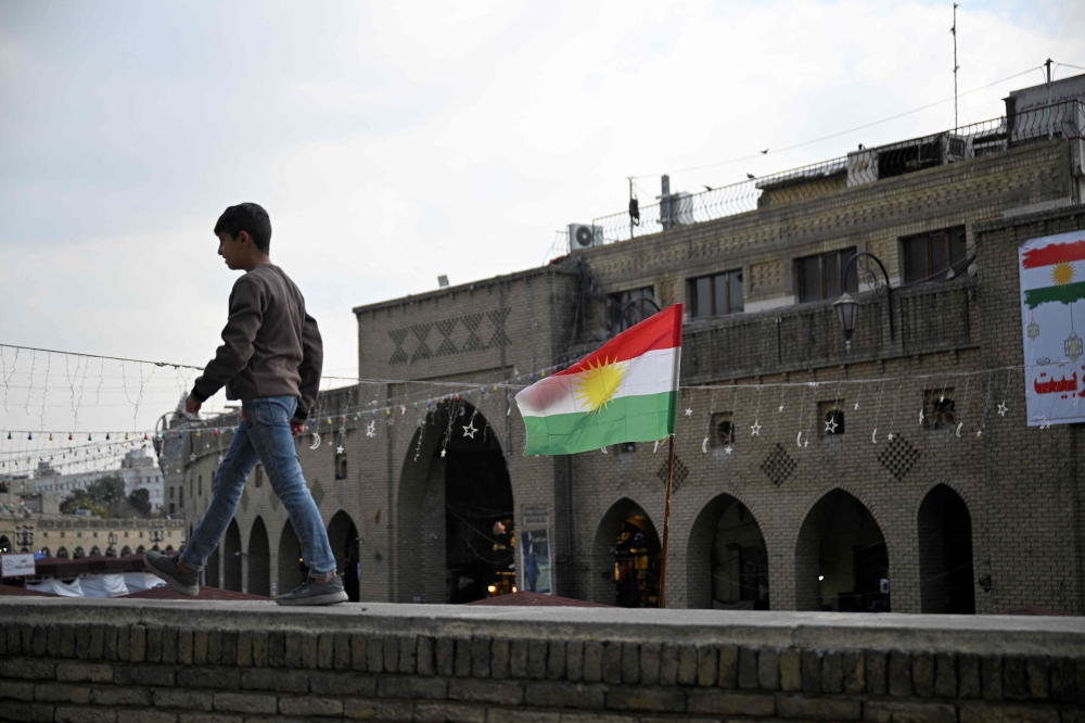 A youth walks on the precipice of a wall, past the Kurdish flag, in Erbil, the capital of Iraq's autonomous Kurdish region. — AFP pic