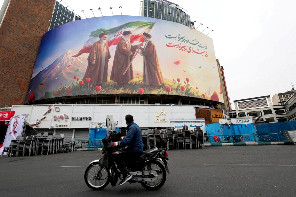 A man on a motorcycle looks at a large billboard featuring Iran’s new Supreme Leader Mojtaba Khamenei, and late Supreme Leaders Ayatollah Ali Khamenei and Ayatollah Ruhollah Khomeini, amid the US-Israeli conflict with Iran, in Tehran March 12, 2026. — Reuters pic