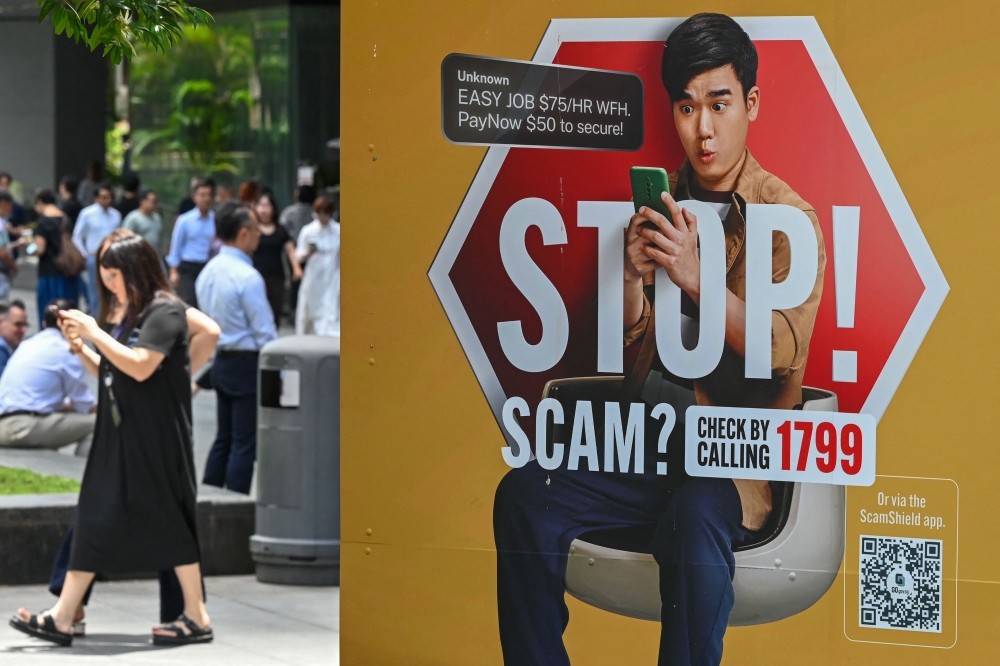 People walk past a poster warning of online scam threats in the Raffles Place financial business district in Singapore. The republic has stepped up its crackdown on scammers as cases and losses have soared in recent years. — AFP pic