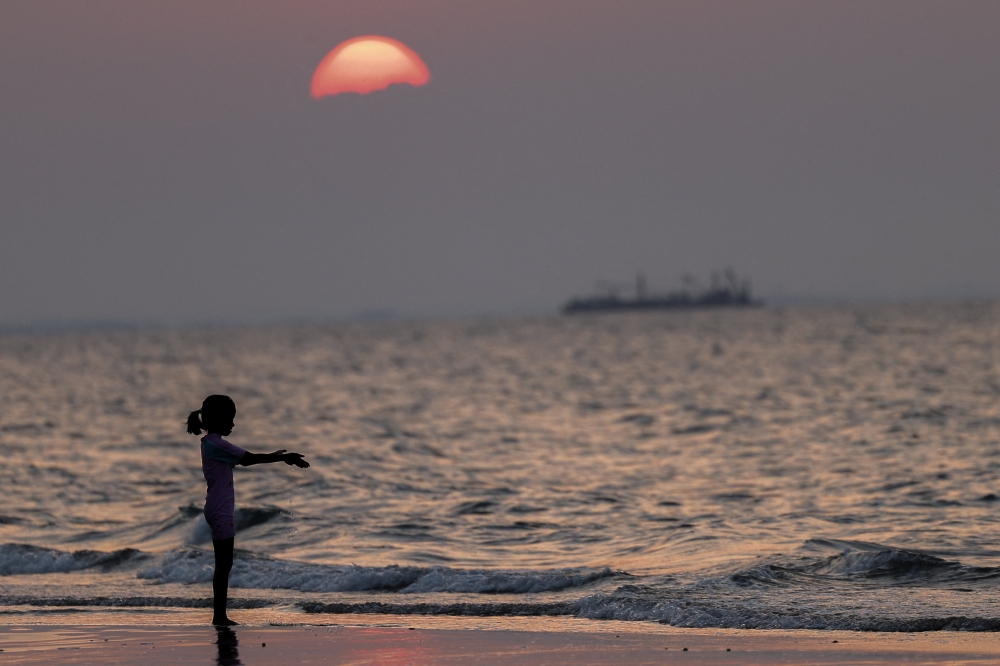 A child plays on Qurum Beach at sunset as vessels sit at anchor in the background, amid the US-Israeli conflict with Iran, off the shore of Muscat, Oman, March 14, 2026. — Reuters pic