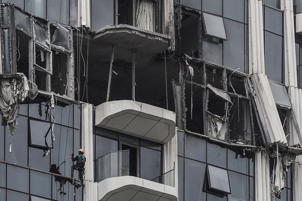 A steeplejack assesses the damage after a building was hit by a reported drone strike in Dubai’s Creek Harbour on March 12, 2026. — AFP pic