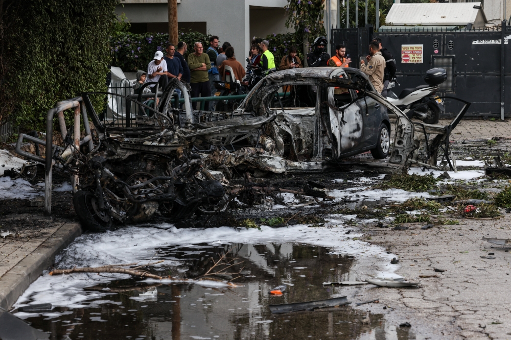 People gather near destroyed vehicles following an Iranian projectile strike in central Israel on March 15, 2026, amid the ongoing US-Israeli conflict with Iran. — Reuters pic