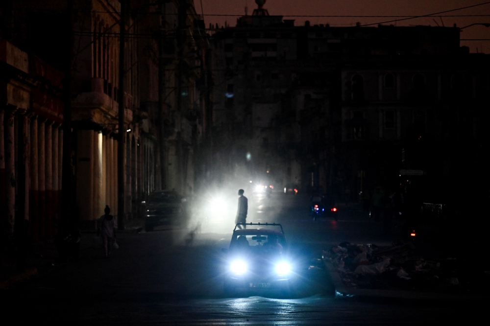 A man walks while cars cruise along a street during a blackout in Havana on March 16, 2026. — AFP pic