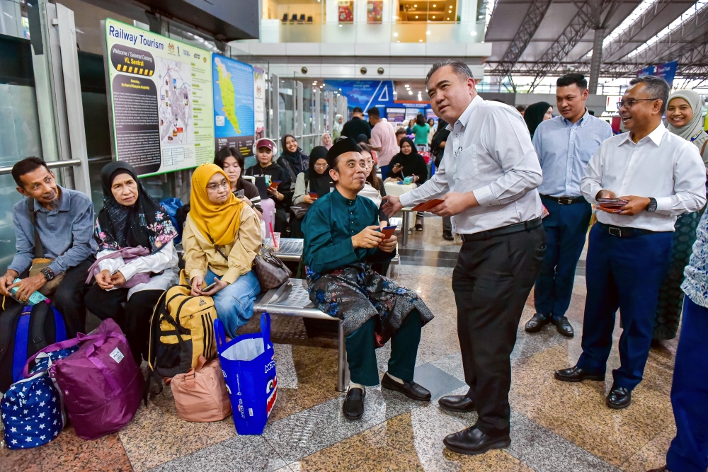 Transport Minister Anthony Loke (standing, centre) distributes Raya 2026 gift packs to KTMB passengers at KL Sentral on March 17, 2026. KTMB is providing 196 extra ETS trips and 10 new trains get Malaysians home faster for Raya this year. — Bernama pic