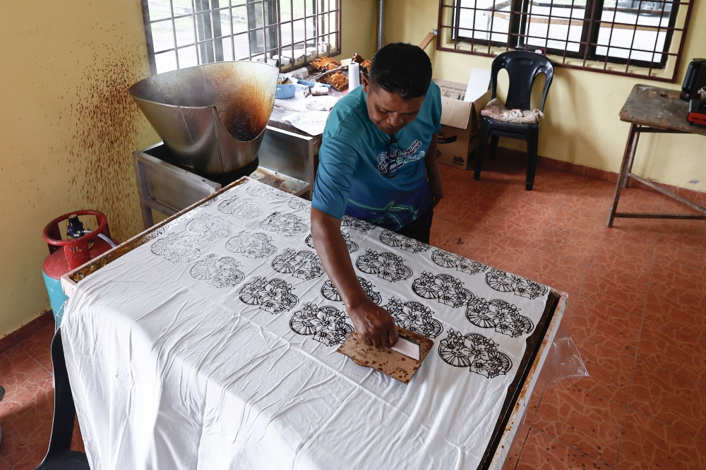 A worker carries out the batik stamping process using bullock‑cart wheel and kesidang flower motifs during a visit to the Felda Hutan Percha Community Batik Terap Craft Product Development and Production Workshop in Alor Gajah March 18, 2026. — Bernama pic