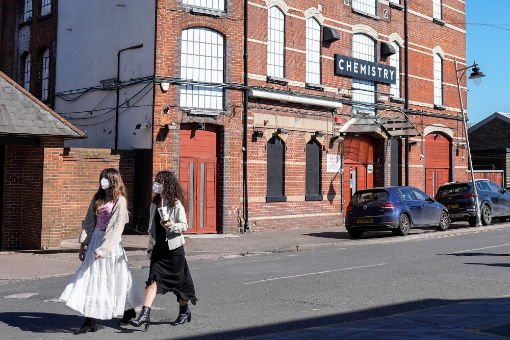 Pedestrians (left) wearing face masks walk past Club Chemistry (right), a nightclub linked to a recent outbreak of meningitis in Canterbury, south-east England on March 18, 2026. 