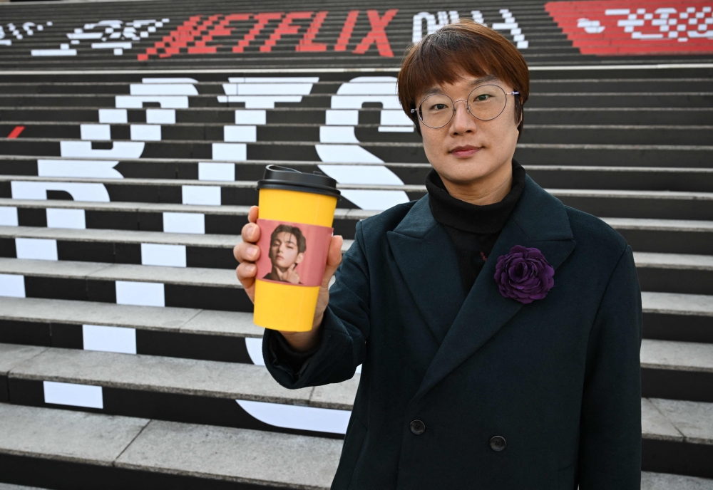 Traditional Korean artist Sung Young-rok, a fan of K-pop boy group BTS, poses with a cup holder featuring a photo of BTS member V in front of the stairs displayed with the BTS logo at Gwanghwamun Square in Seoul March 10, 2026. — AFP pic