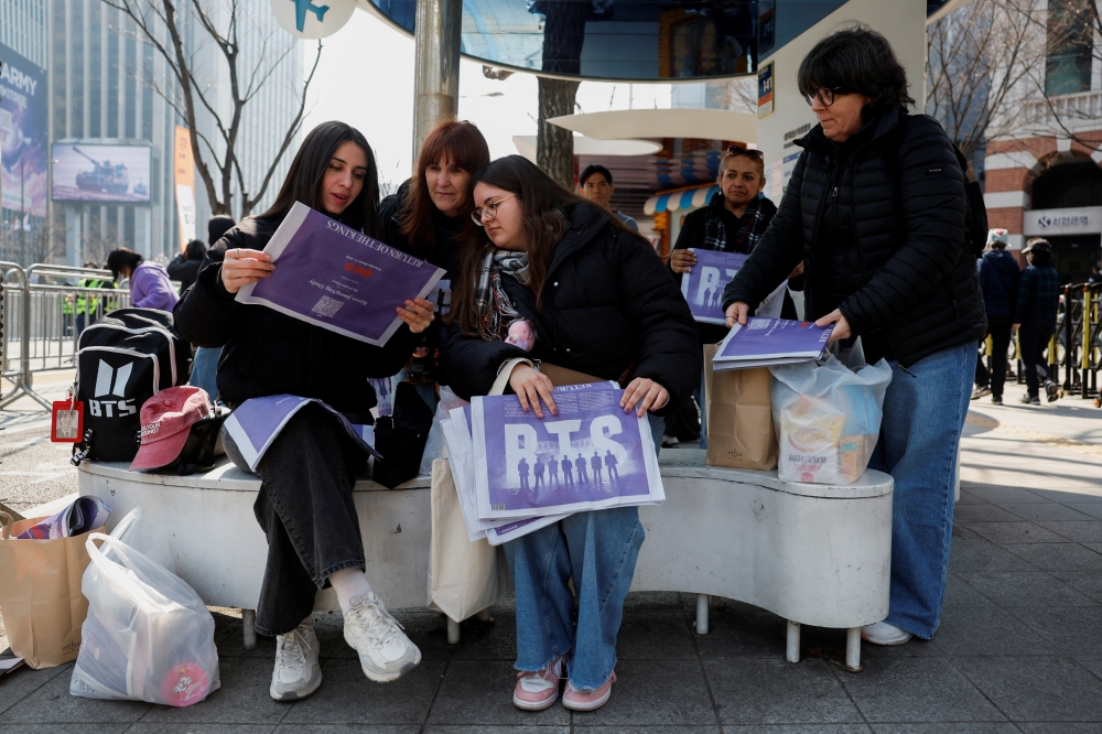 Fans of Kpop group BTS read BTS special edition newspapers on the day of the ‘BTS The Comeback Live Arirang’ concert, outside the concert venue, in central Seoul, South Korea, March 21, 2026. — Reuters pic
