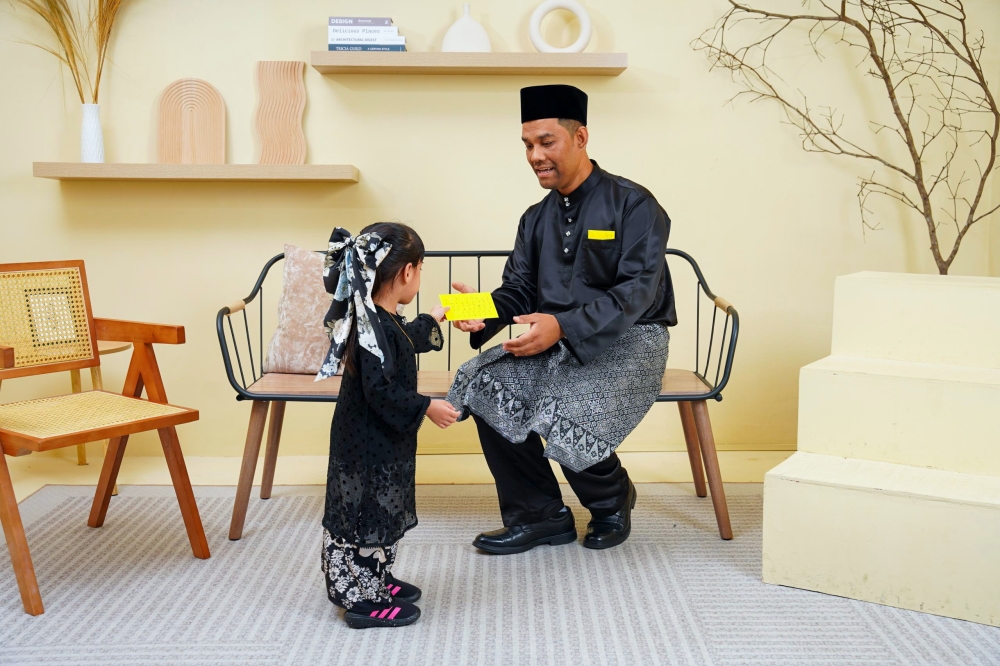 Mohd Armi Rusli (right) hands duit raya to his daughter, Naura Aleena, using envelopes printed with Malaysian Sign Language (BIM). — Bernama pic