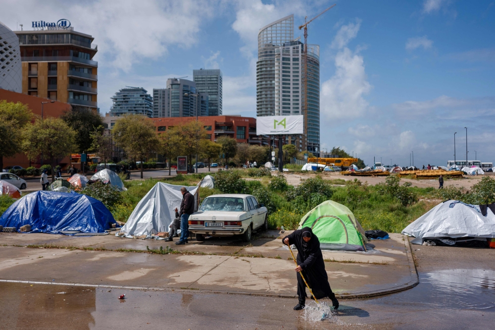 A displaced woman pushes water out of a puddle after a night rainstorm in an unofficial camp, erected along Beirut’s seafront area on March 20, 2026. — AFP pic