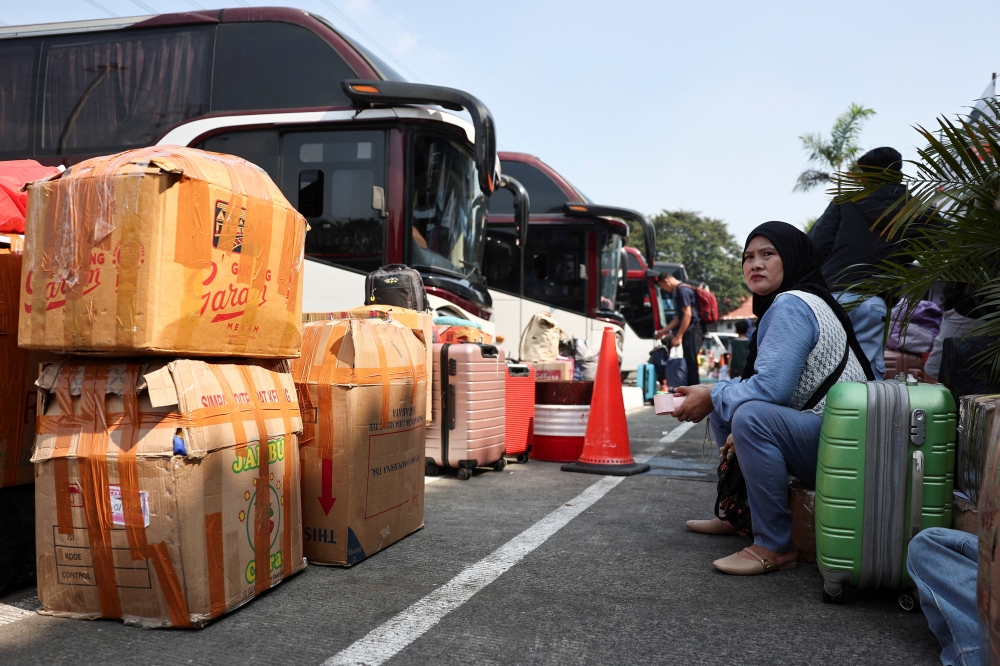 A woman sits next to luggage while waiting for a bus at a terminal during the annual Eid al-Fitr homecoming exodus known locally as 