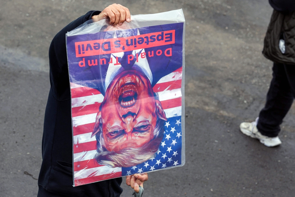 A mourner holds a cartoon denouncing the US President Donald Trump and associating him with the late convicted US sex offender Jeffrey Epstein, during the funeral ceremony for Iran’s slain intelligence minister Esmail Khatib and his family after the weekly Friday Muslim noon prayers in Tehran on March 20, 2026. — AFP pic