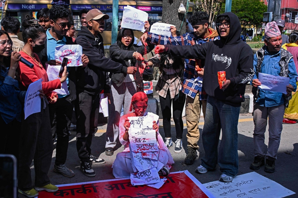 Activists spatter a woman with red powder to symbolise blood during a protest demanding the release of the inquiry report by a Nepal government investigation commission probing the September 2025 youth-led uprising that toppled the government, in Kathmandu March 22, 2026. — AFP pic