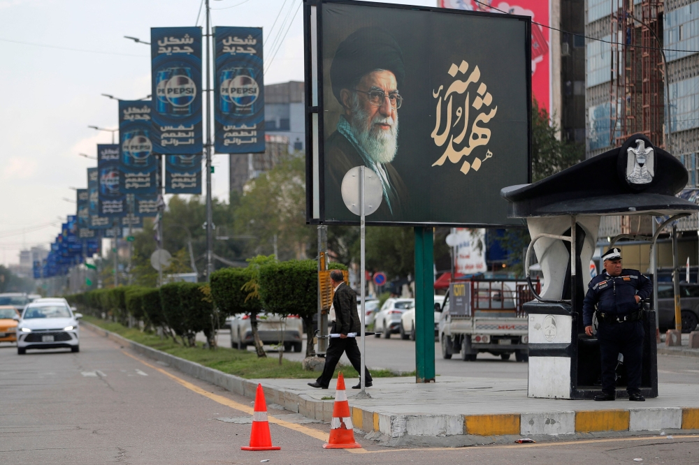 An Iraqi police officer stands guard as a man walks beneath a billboard bearing a portrait of Iran’s slain supreme leader Ayatollah Ali Khamenei in Baghdad on March 25, 2026. — AFP pic
